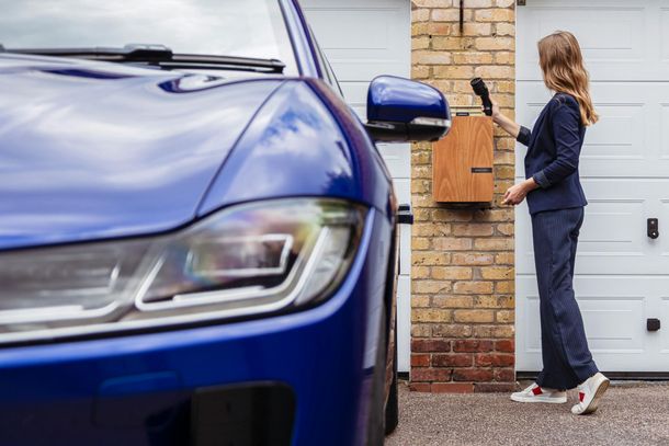 A woman is standing next to a blue car in front of a garage door.