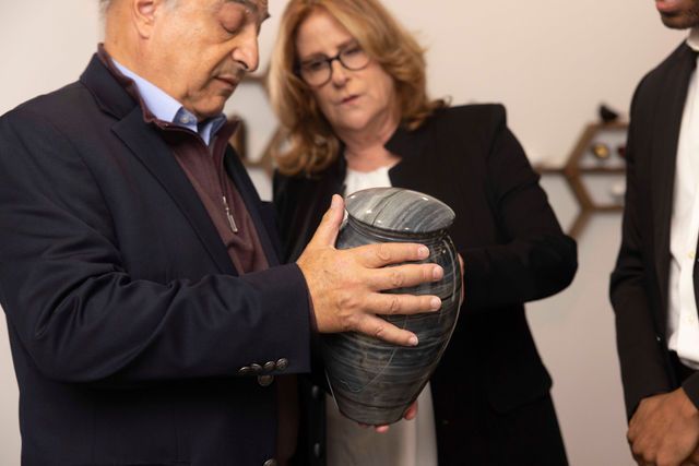 A man in a suit is holding a vase while a woman looks on.