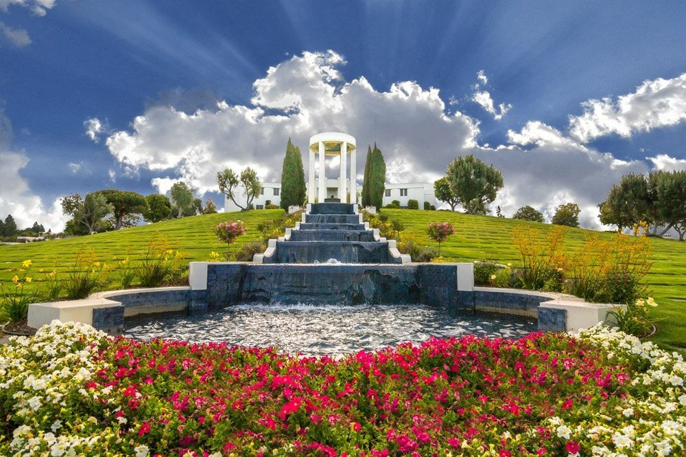 A waterfall in a garden with flowers and a gazebo in the background