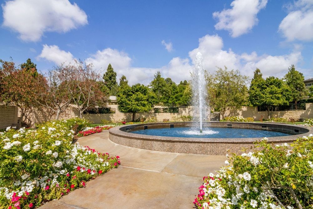 There is a fountain in the middle of a garden surrounded by flowers.