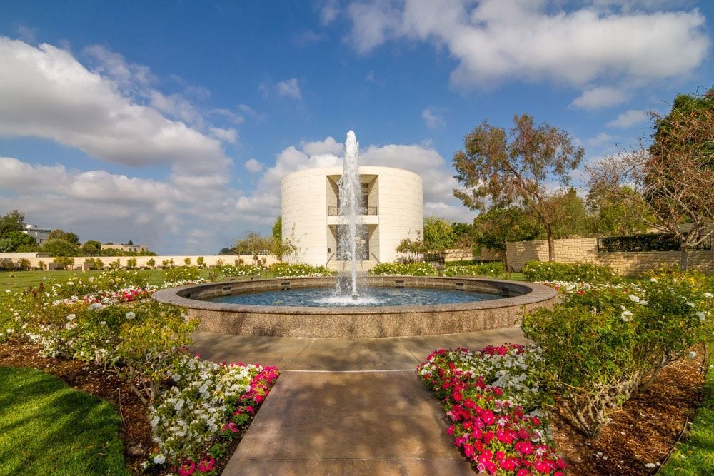 There is a fountain in the middle of a garden in front of a building.