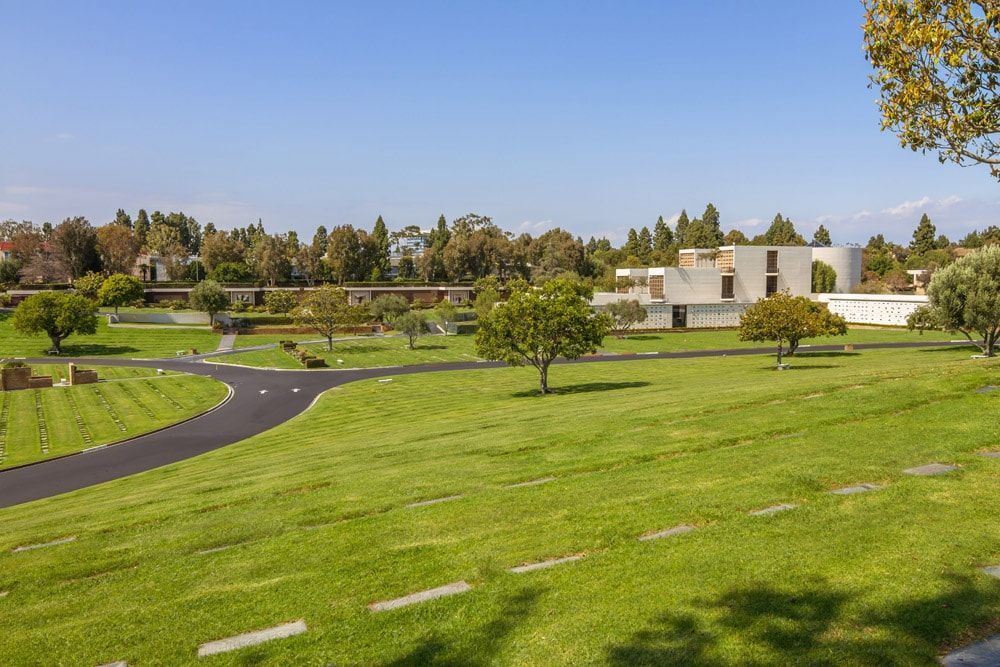 A cemetery with a lot of grass and trees and a building in the background.