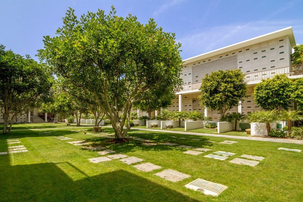 A lush green lawn with trees in front of a building sacred cemetery grounds Hillside