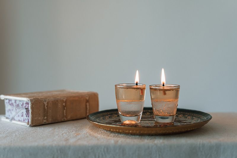 Two lit candles are on a tray on a table next to a book.