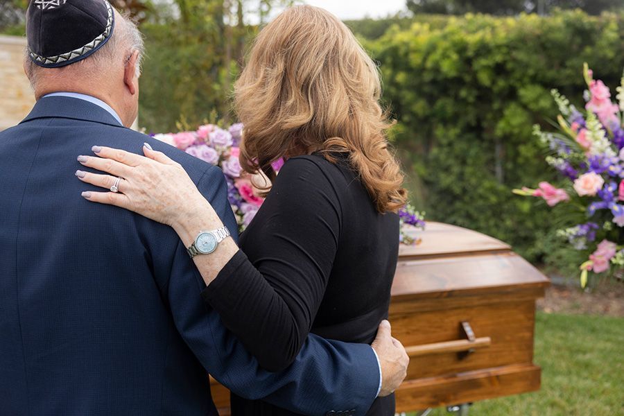 A man and a woman are standing next to a coffin at a funeral.