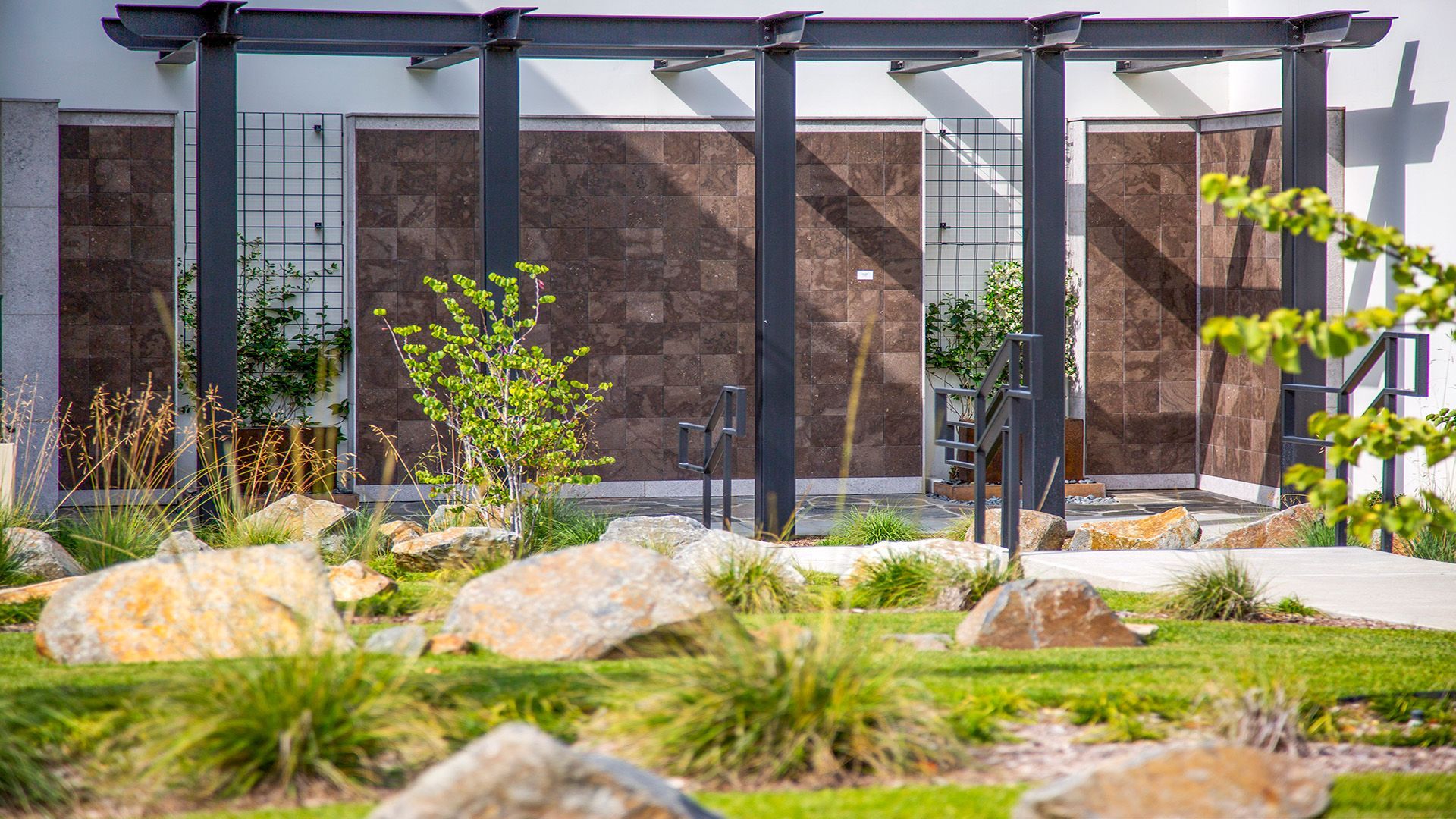 A pergola is sitting in the middle of a lush green garden in front of a building. Hillside Memorial Park