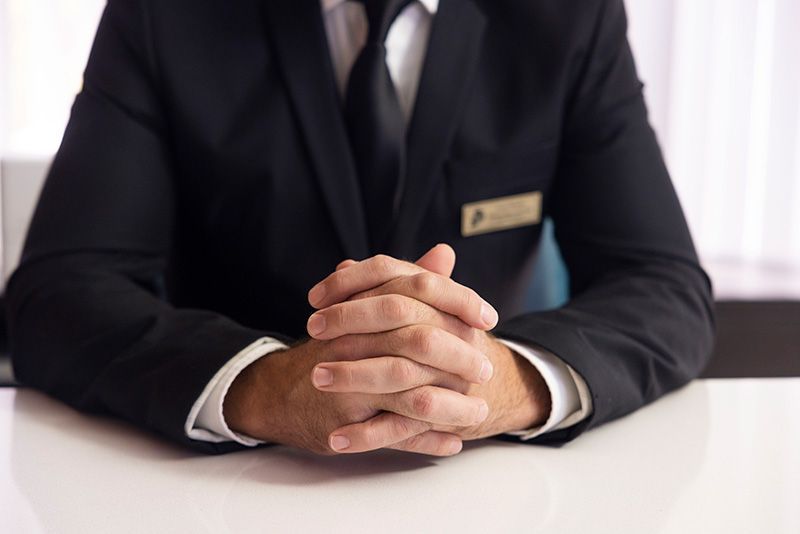 A man in a suit and tie is sitting at a table with his hands folded.