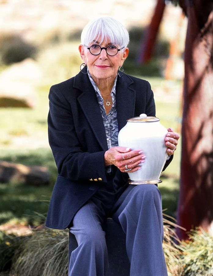 A woman is sitting on a rock holding a white urn