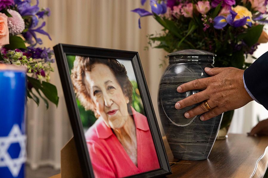 A man is holding an urn next to a picture of an elderly woman.