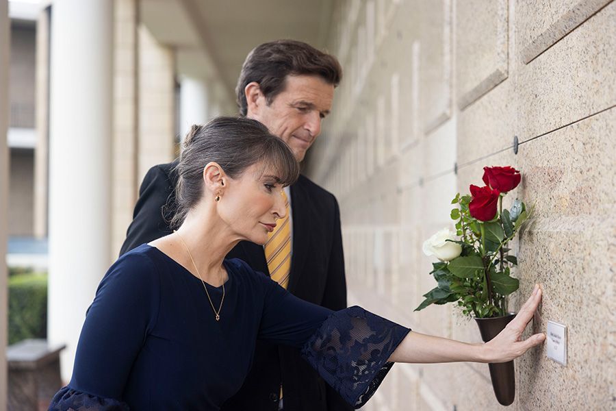 A man and a woman are putting flowers in a vase in a cemetery.