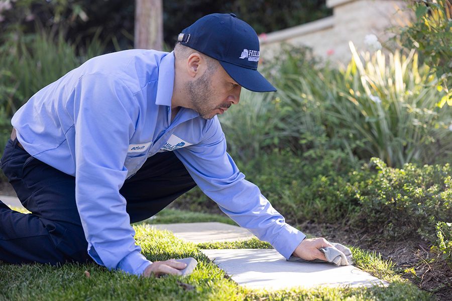 A man in a blue shirt and hat is kneeling on the grass cleaning a gravemarker