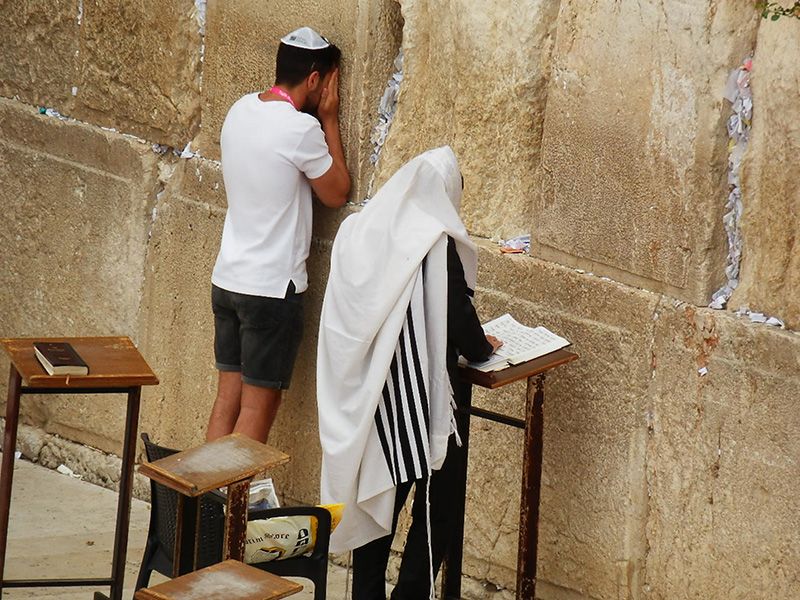 A man is kneeling down in front of a wall and praying.