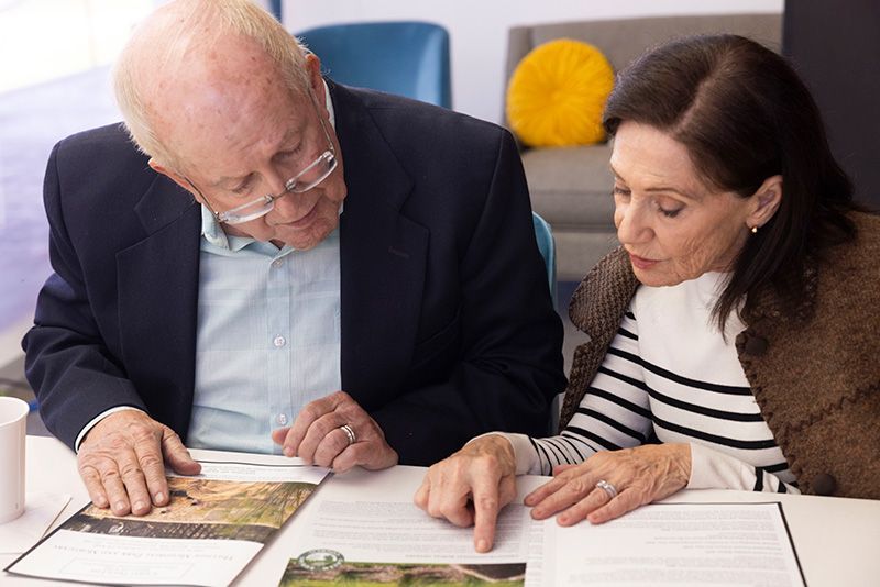 A man and a woman are sitting at a table looking at a book.