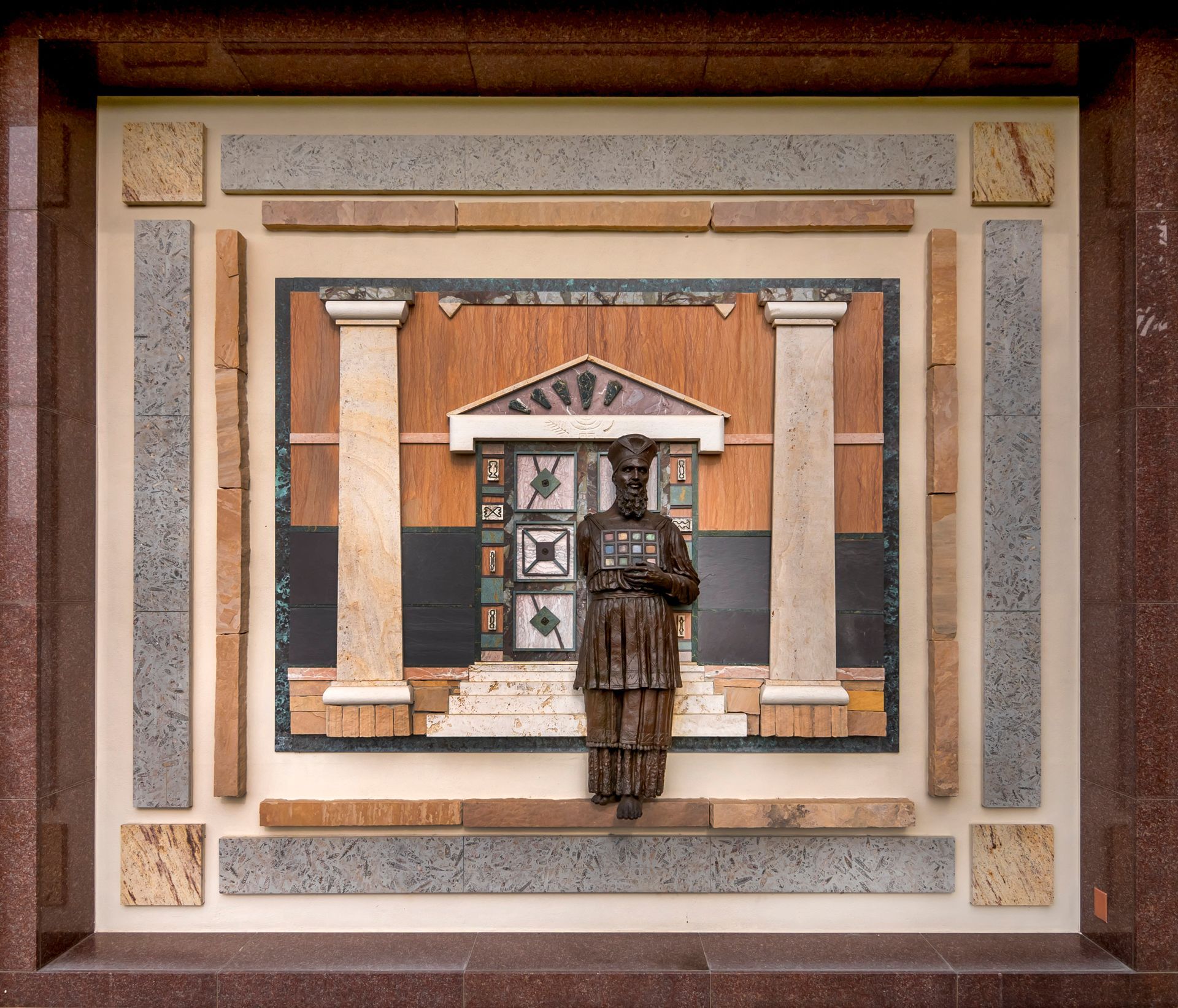 Stone carving of a man in front of a structure with columns; surrounded by stone tiles.