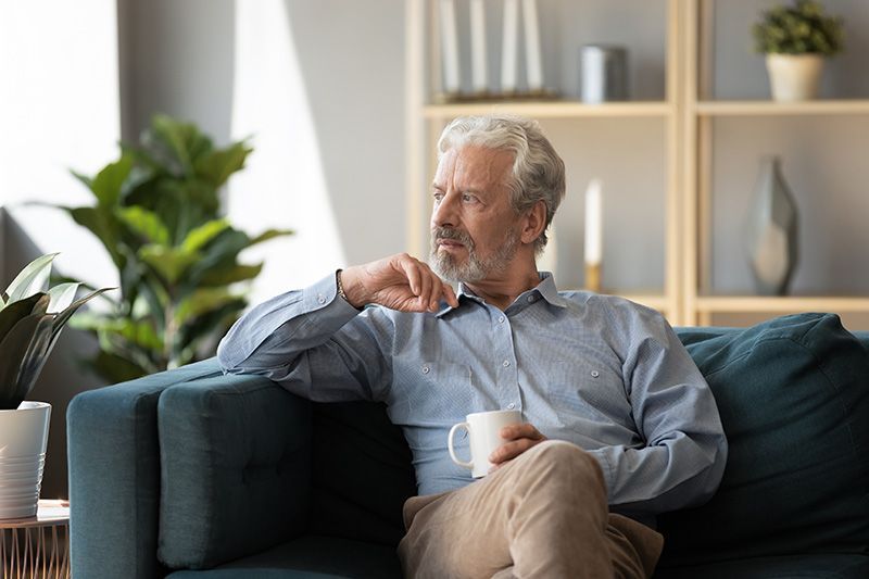 An older man is sitting on a couch holding a cup of coffee.