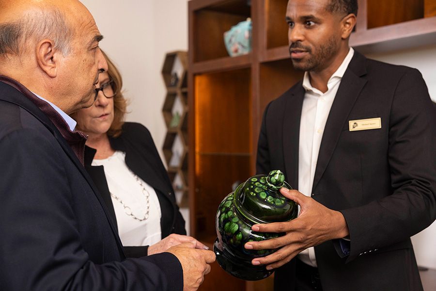 A man in a suit is holding a green cremation urn in front of a group of people.