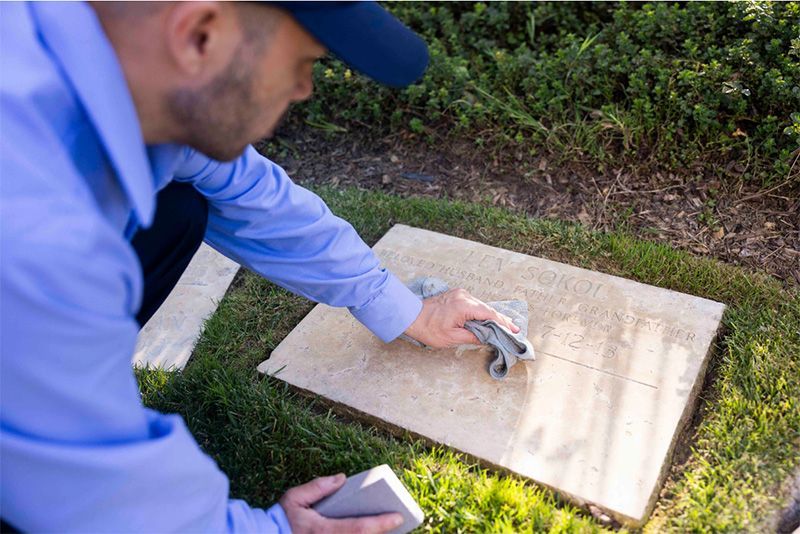 Staff worker at Hillside Memorial Park and Mortuary in CA cleaning off grave marker