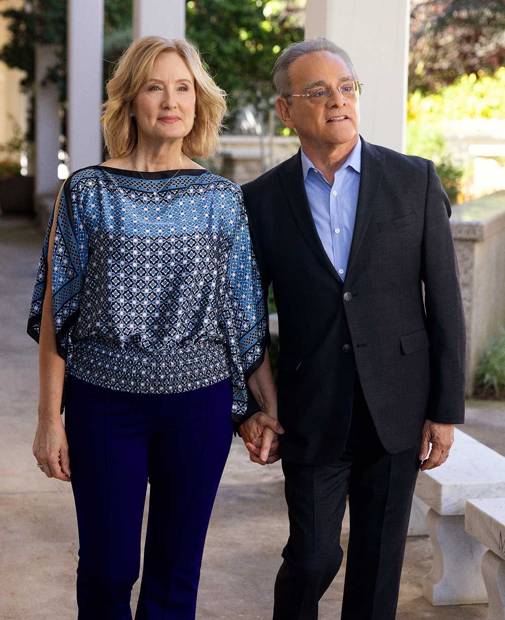 A well-dressed couple holds hands while walking outdoors.