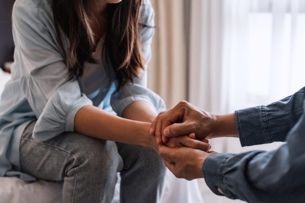 A man is holding a woman 's hand while sitting on a bed.