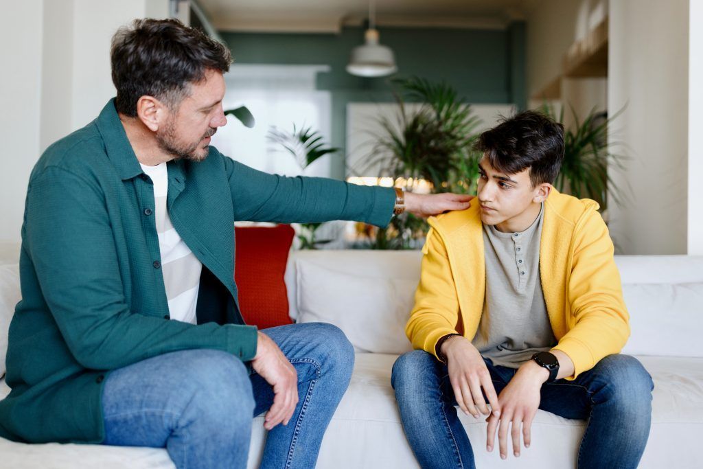 A man and a boy are sitting on a couch talking to each other.