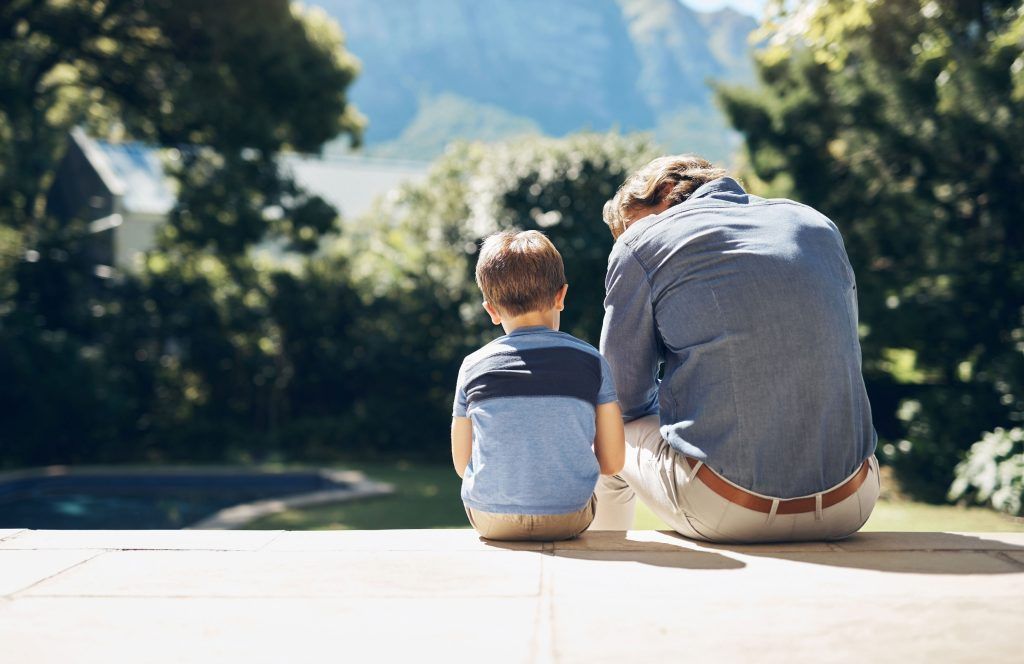 A man and a boy are sitting on a deck looking at the mountains.