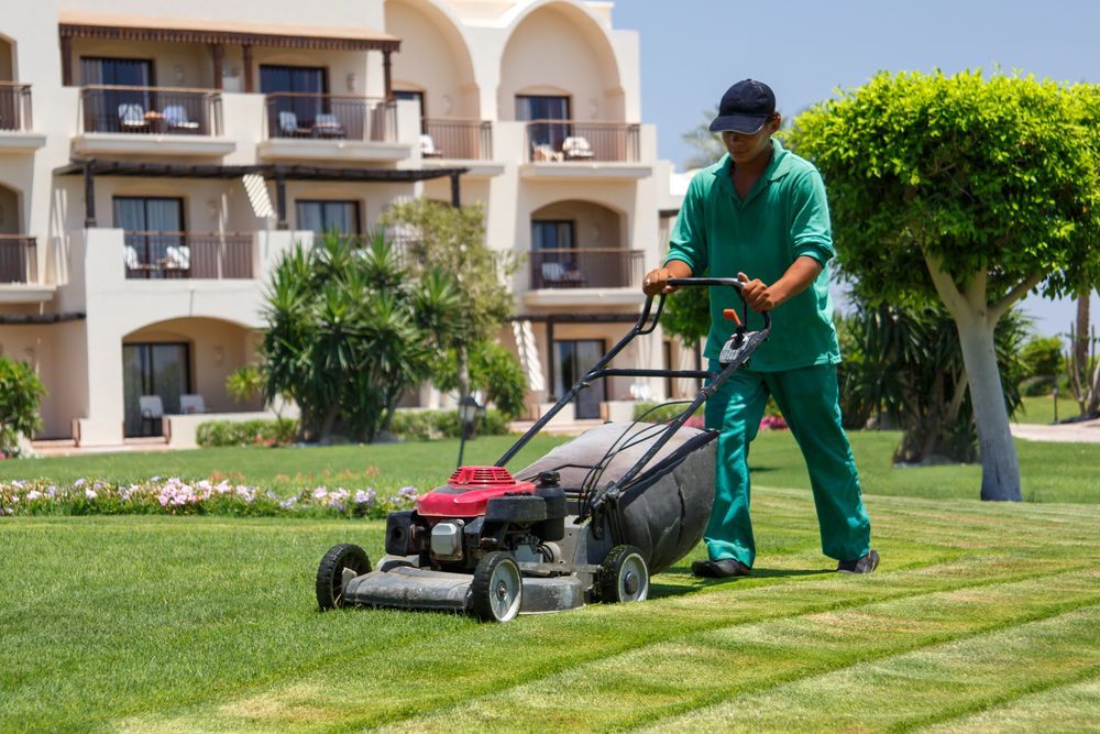 Worker mowing a green lawn in front of an apartment building