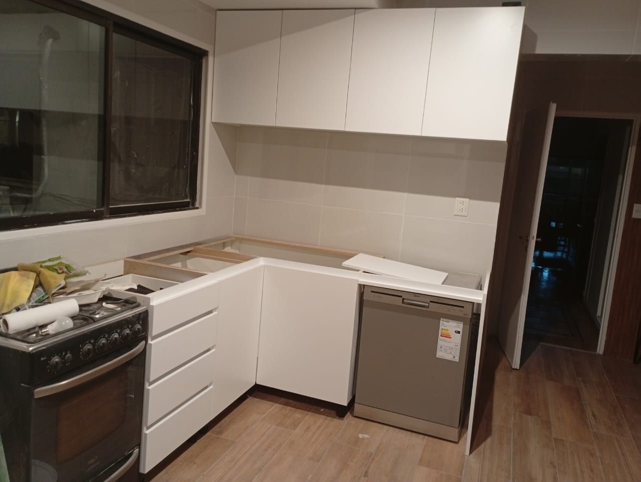 Gabinetes de cocina blancos con lavavajillas y estufa, en construcción cerca de una ventana.