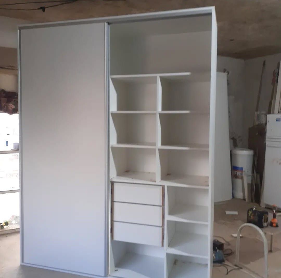 Armario empotrado blanco con puerta corredera y estantes, cajones y almacenaje abierto en una estancia.