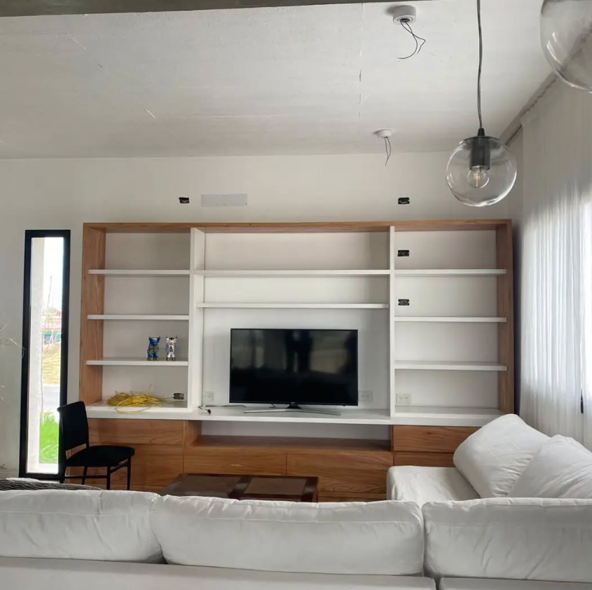 Sala de estar con un centro multimedia de madera, estantes y un sofá blanco.