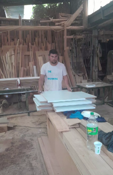 Un hombre en un taller sostiene paneles blancos, rodeados de madera.