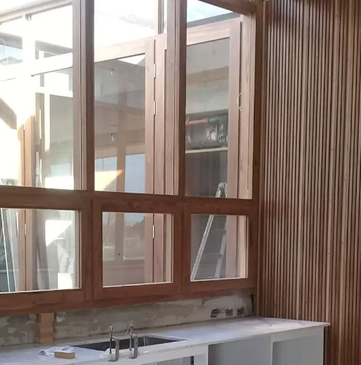 Ventanas con marco de madera y pared de paneles de madera, con encimera y lavabo blancos.
