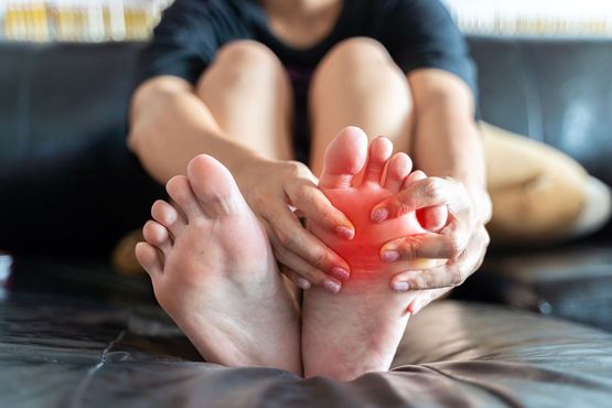 Woman seated on a couch holding her foot, indicating pain with red highlight.