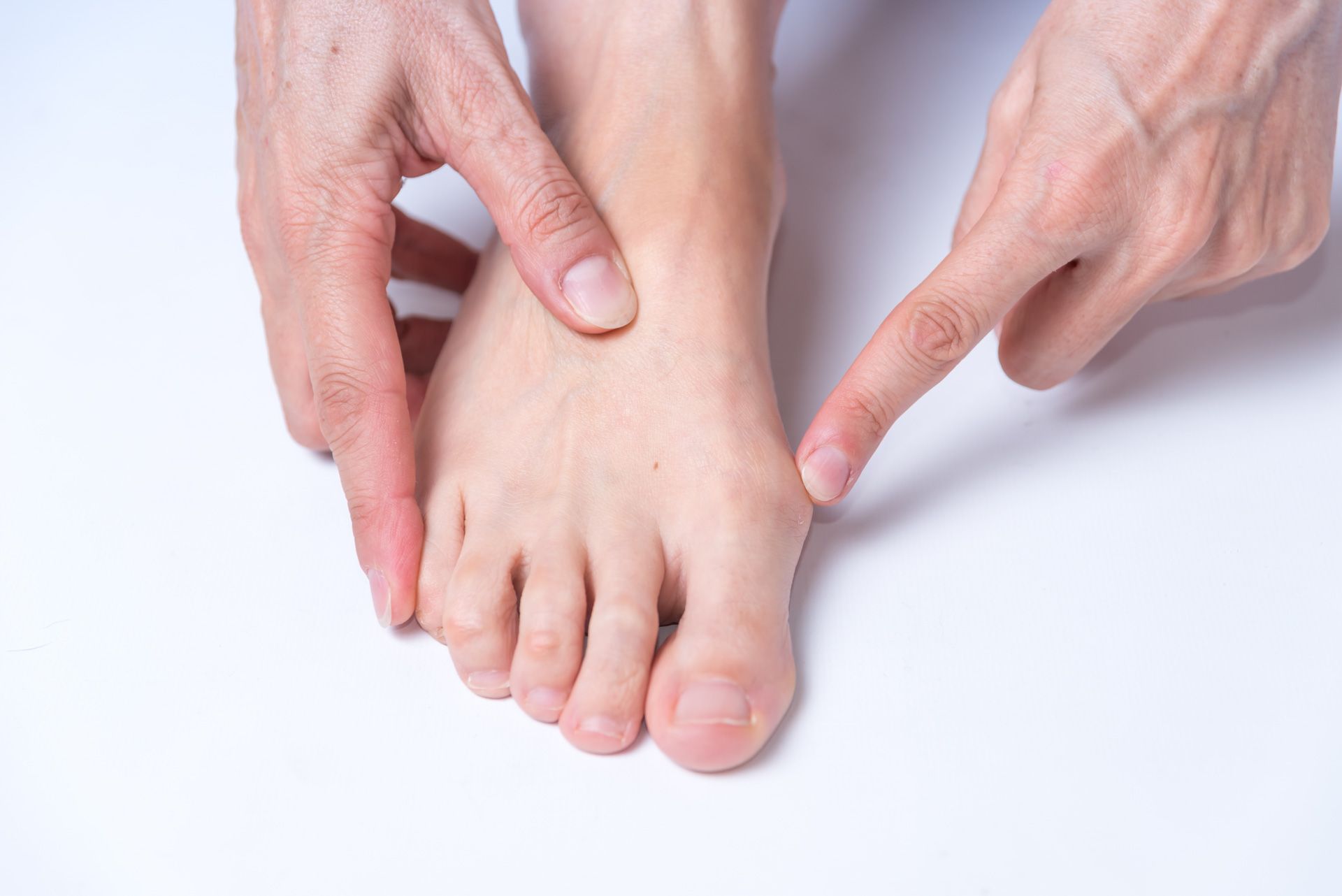 Person's foot with hand pointing to the big toe joint, possibly indicating a bunion or discomfort.