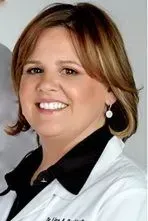 Smiling woman with brown hair and a white coat; wearing pearl earrings.