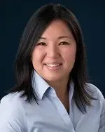 Woman with dark hair smiling in a blue shirt against a dark background.
