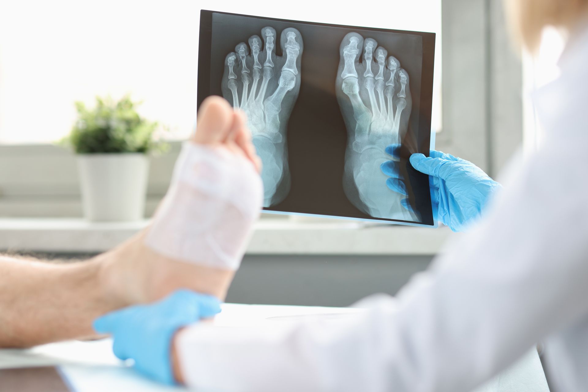 Doctor examining a foot x-ray while treating a patient's bandaged foot in a clinic.