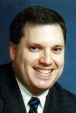 Man with dark hair and a wide smile, wearing a suit and tie.