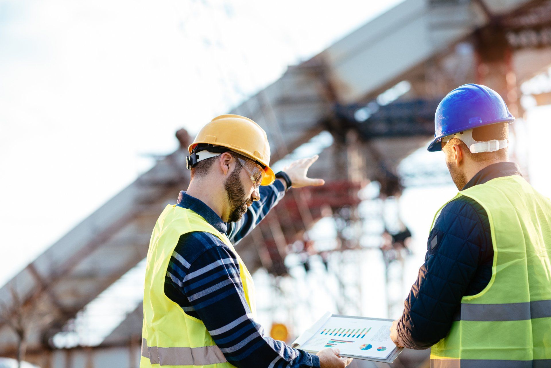 Two construction workers are looking at a tablet at a construction site.