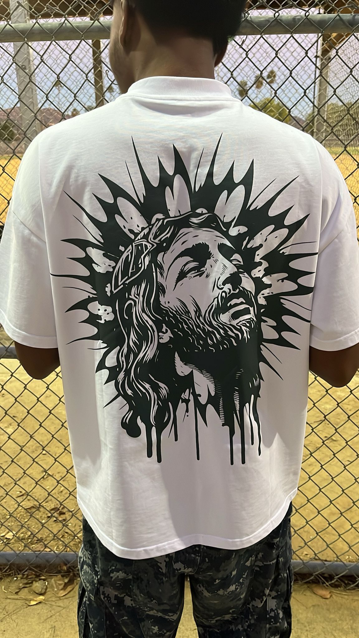 A man is wearing a white t-shirt with a picture of jesus on the back.