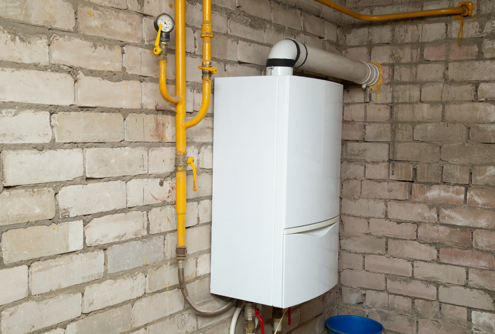 White wall-mounted gas boiler with yellow gas pipes against a brick wall.