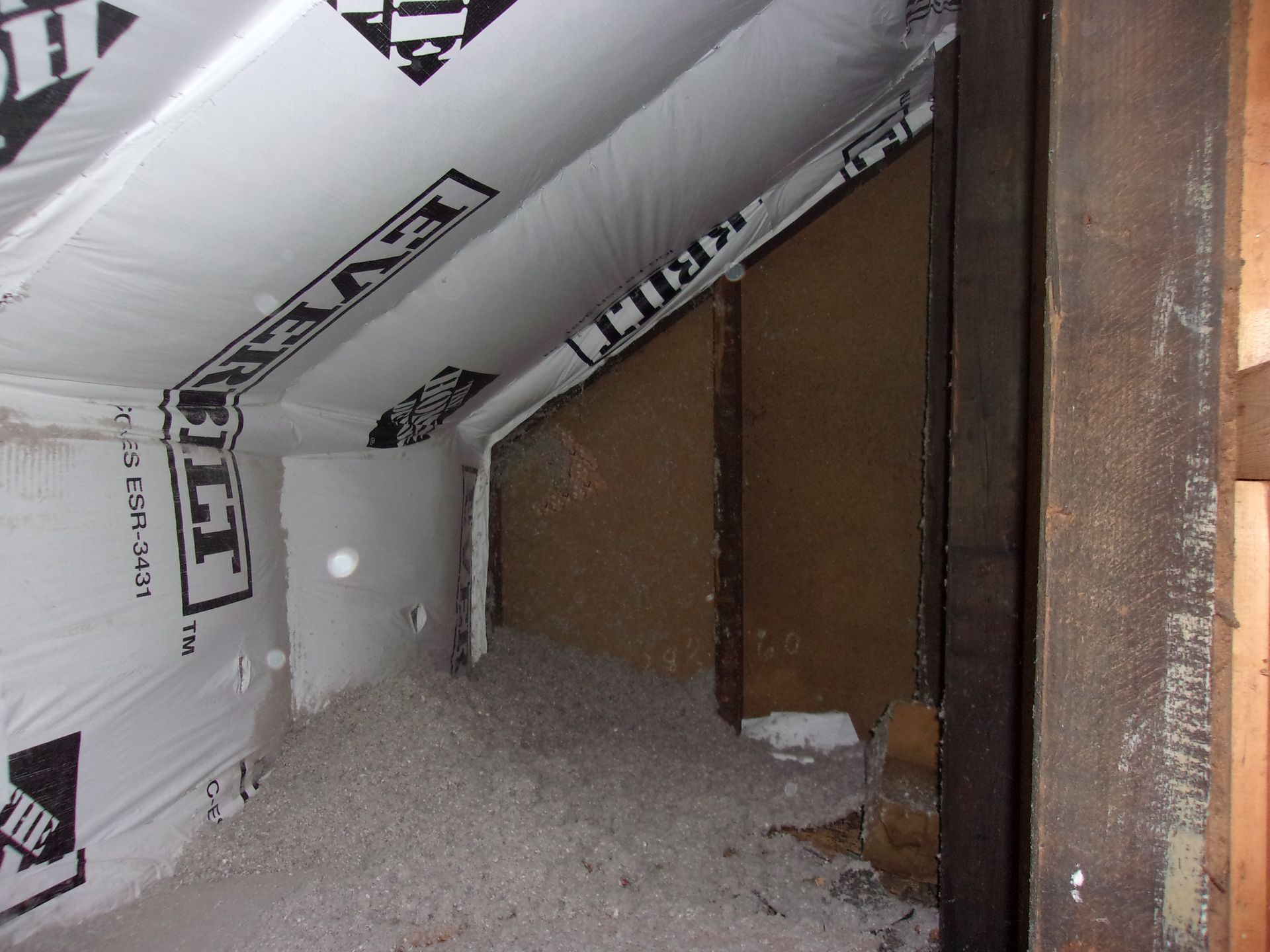Interior of a building under construction with white insulation and a black and white vapor barrier.