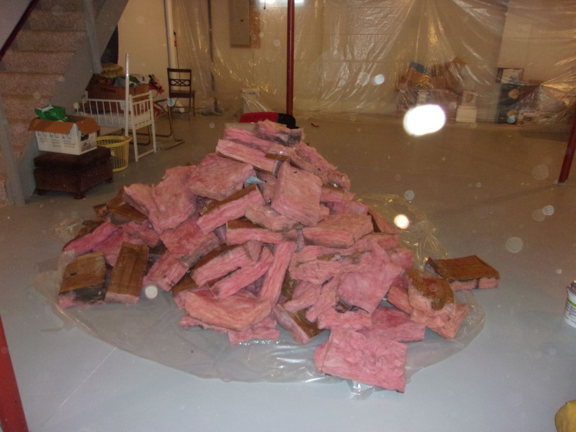 Pile of pink fiberglass insulation on a plastic sheet in a basement, likely for a renovation project.