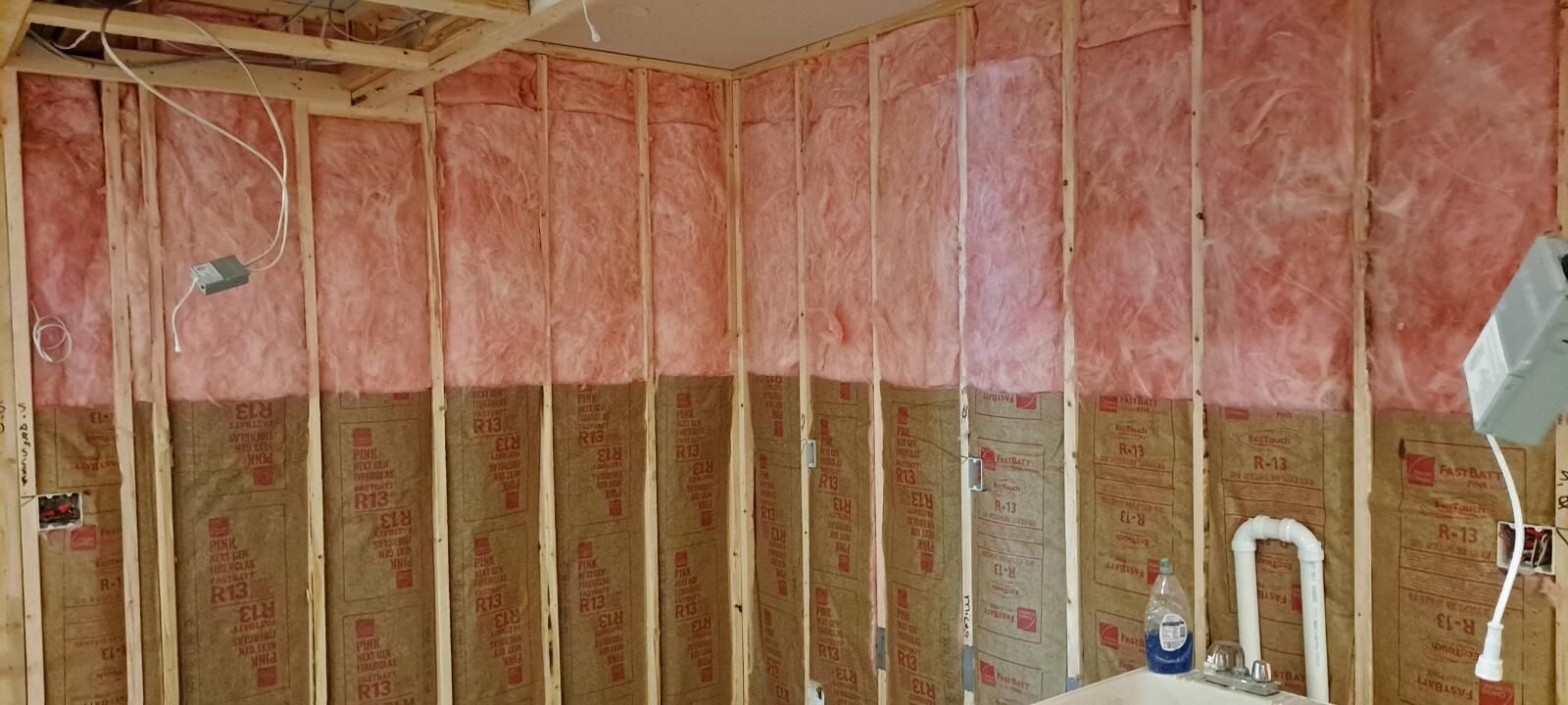 Interior of a room under construction, with wooden studs and pink insulation.