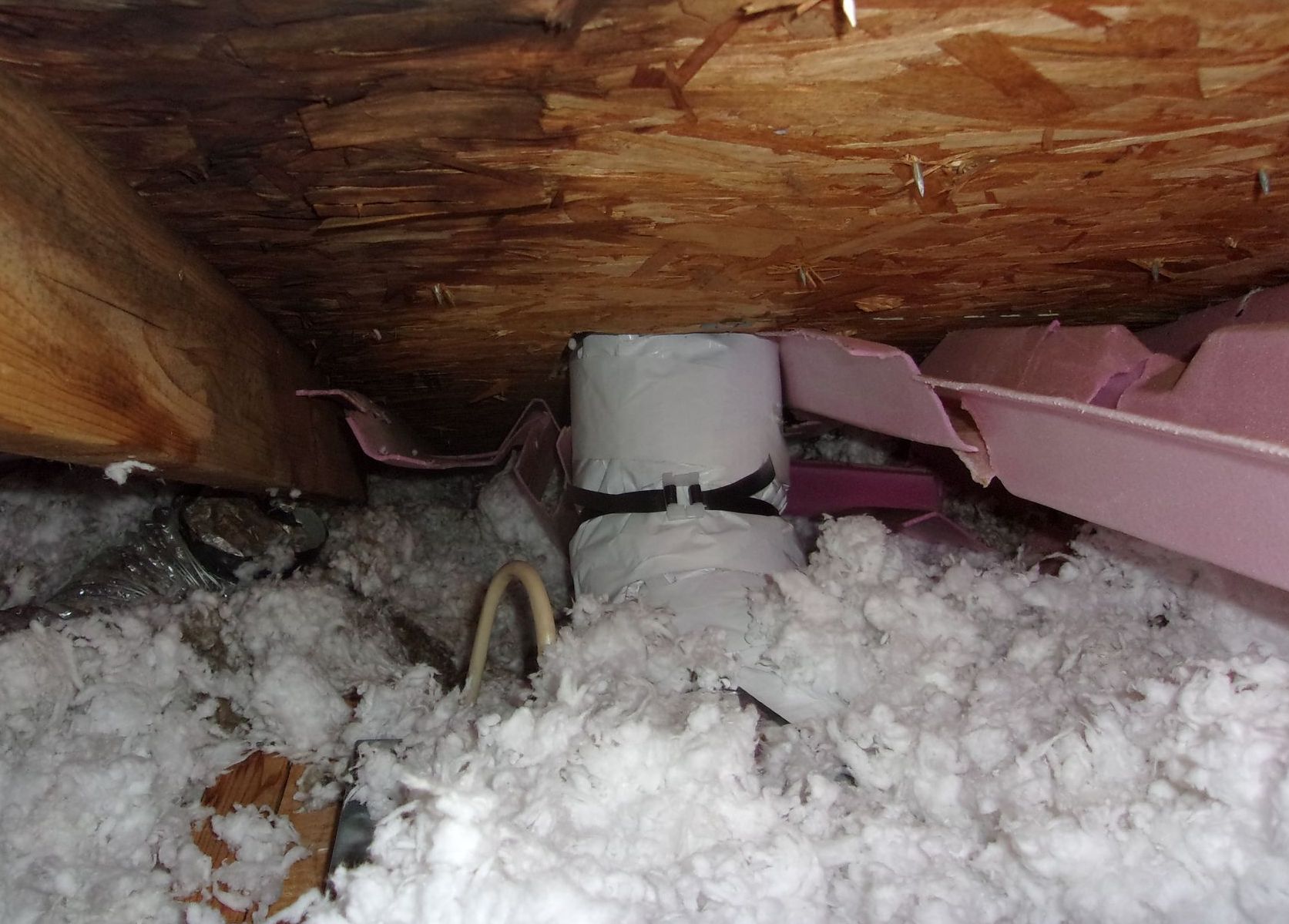 Insulation and a vent pipe in an attic. Pink foam boards are to the right. White insulation surrounds the pipe.