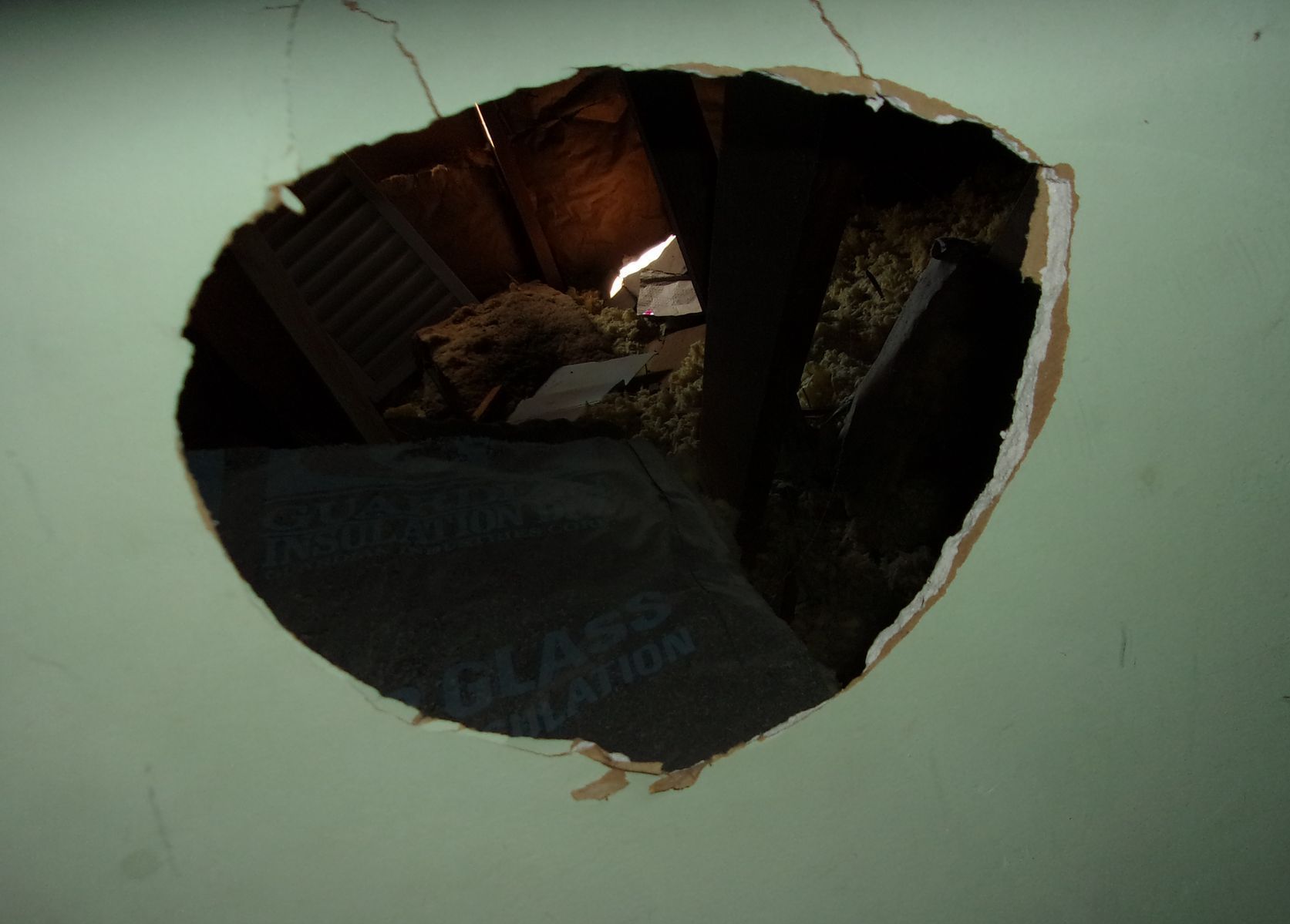 A large hole in a green wall reveals the interior of a building, with visible insulation and debris inside.