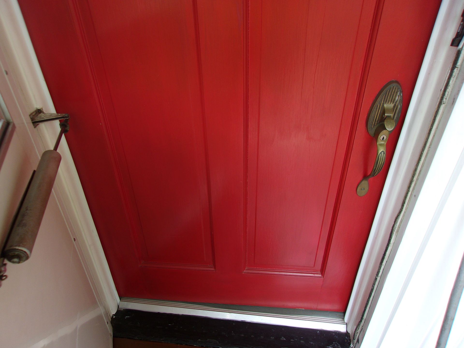Red front door with brass handle and door closer, viewed from below.