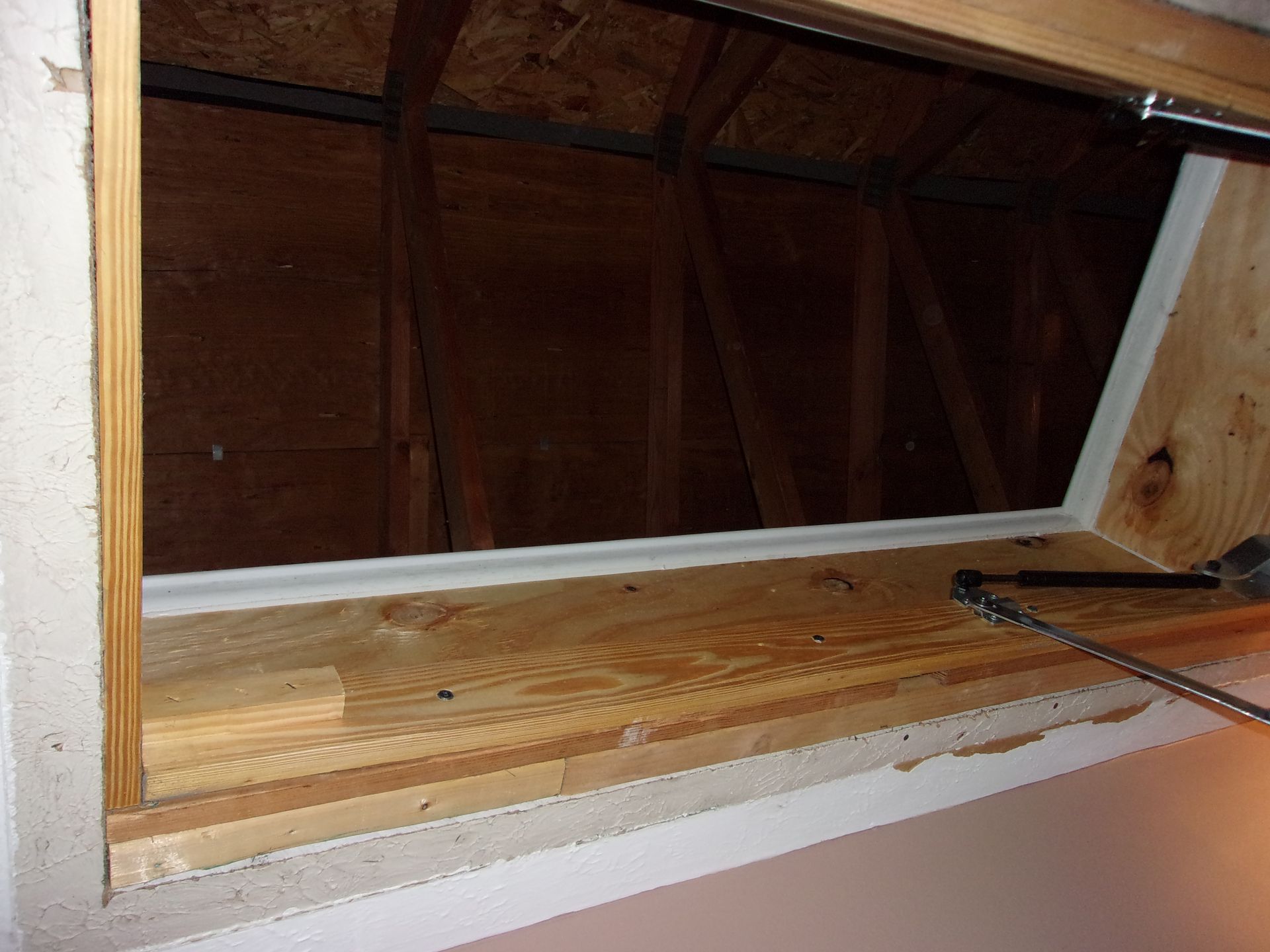 Wooden attic access opening in a ceiling, with a chain and the unfinished attic visible.