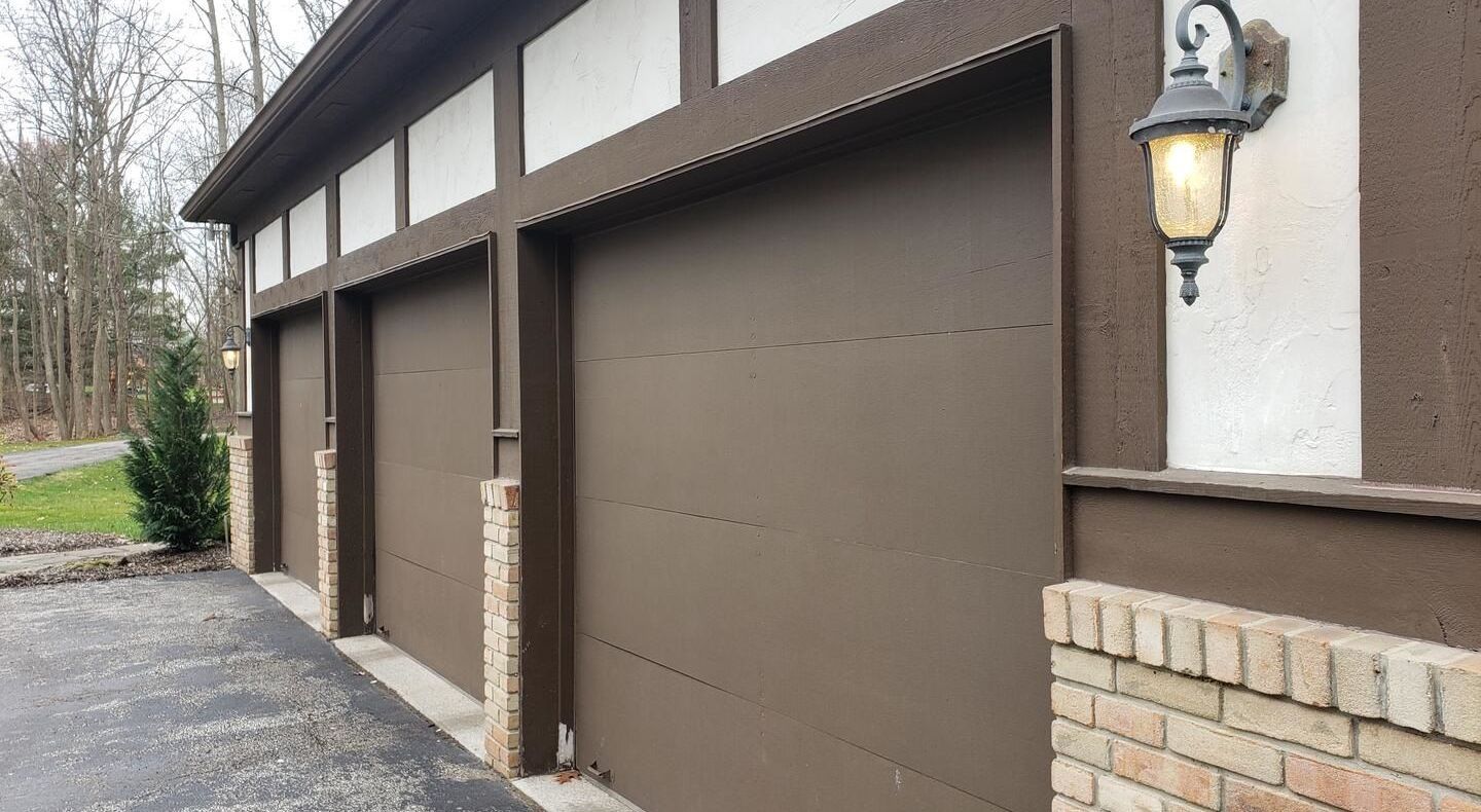 Exterior view of a three-car garage with brown paneled garage doors on a residential home, showcasing clean design and modern curb appeal.