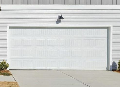 A white garage door is sitting in front of a white house. Unified Insulation Garage Door Services.