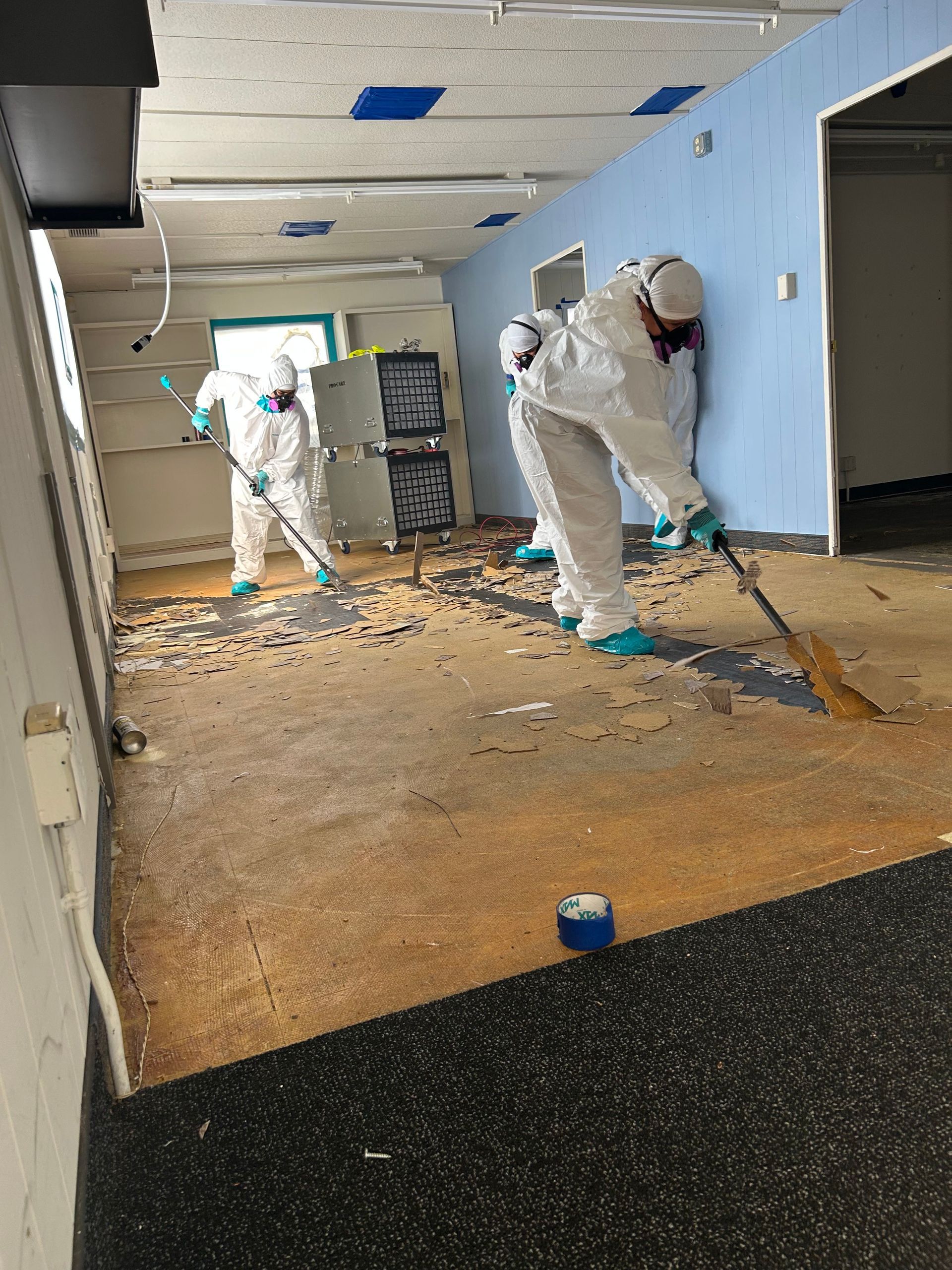Two men in protective suits are cleaning the floor of a room.